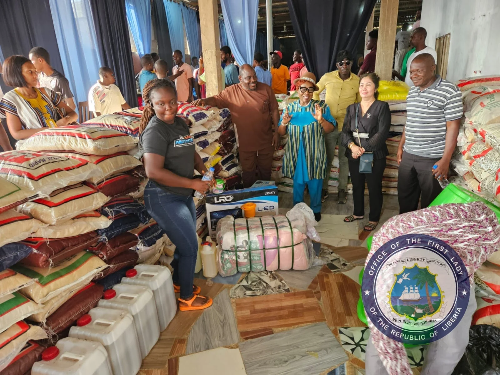 Sacks of rice and relief supplies stacked in a warehouse ahead of distribution, with a delivery team present.